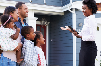 Family looking at woman who is showing them the outside of a house