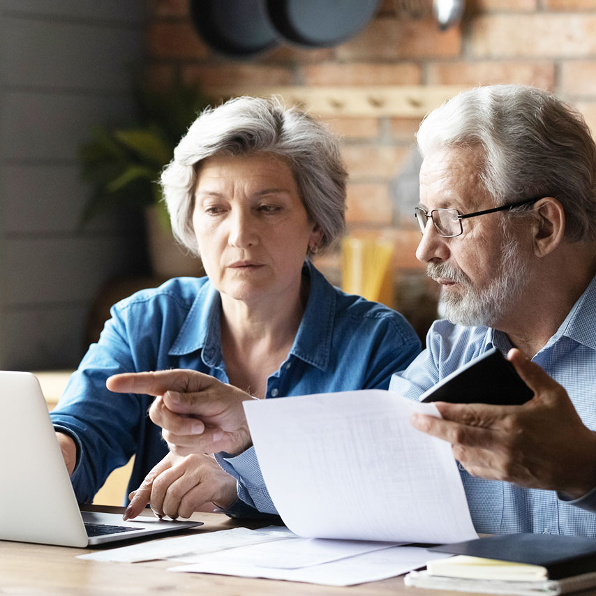 Older woman and man sitting next to each other and looking at paperwork as they pay bills.