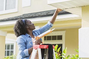 woman fixing her home's gutter
