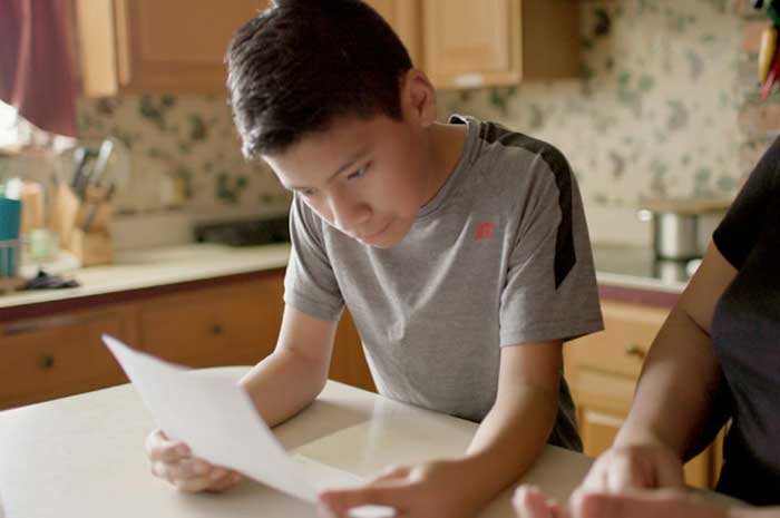 A boy sits next to his family member, looking at a document in order to translate it for her.