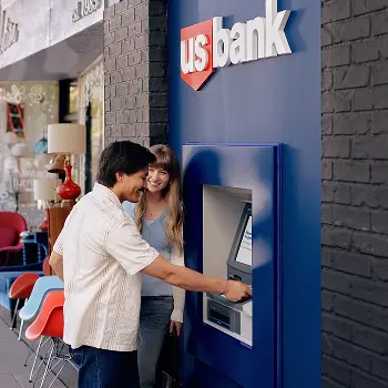 Man using U.S. Bank ATM outside standing next to woman. 