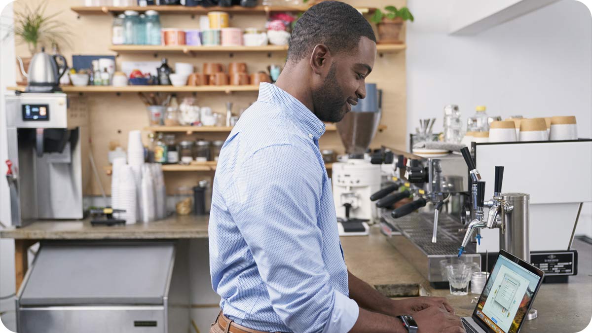 Man working on a laptop computer next to an espresso machine at a coffee shop