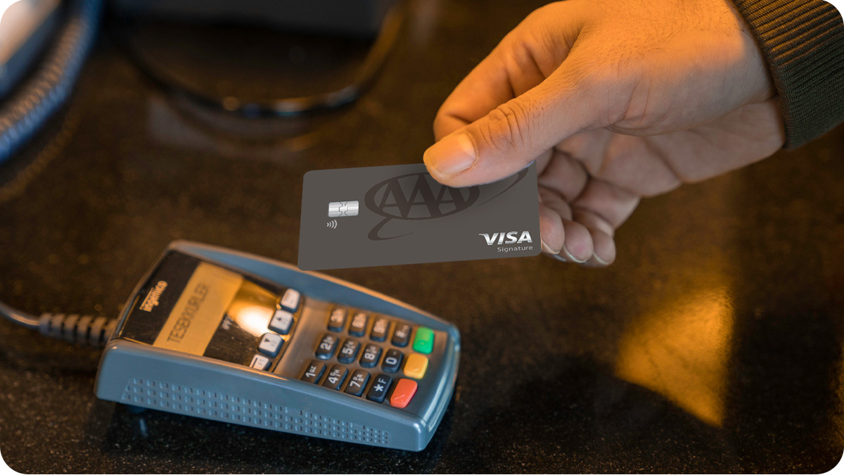 A male hand holding the new AAA card to make a payment at a terminal.