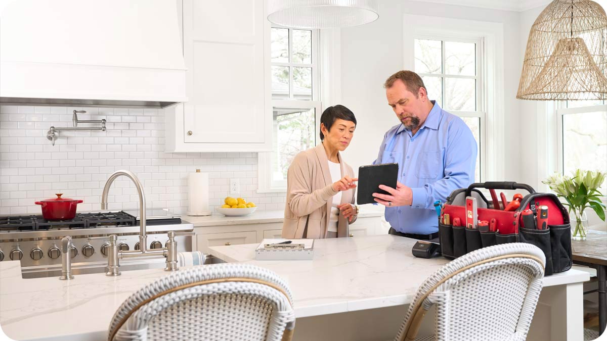 Woman in her kitchen looking at a tablet with a handyman.