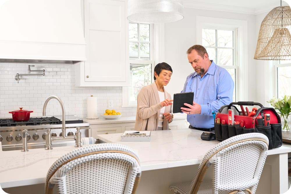 Woman in her kitchen looking at a tablet with a handyman