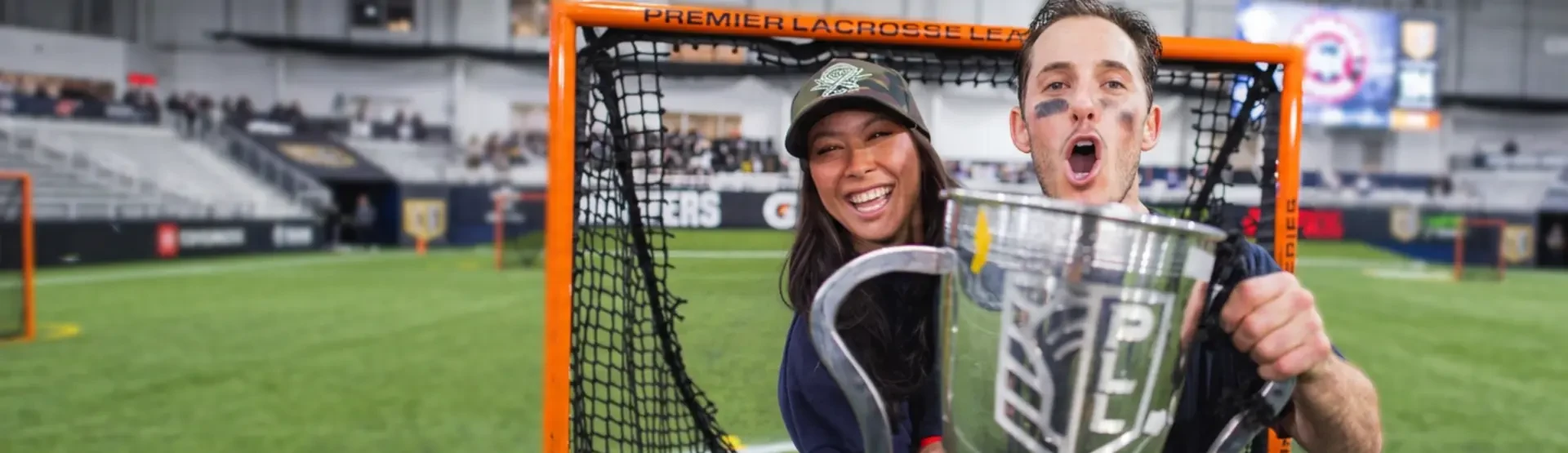 Marcus and Alex Holman standing together on a lacrosse field, smiling and dressed in casual attire.