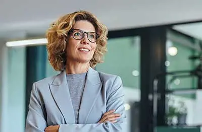 Professionally-dressed woman in glasses is smiling and looking out into the distance.