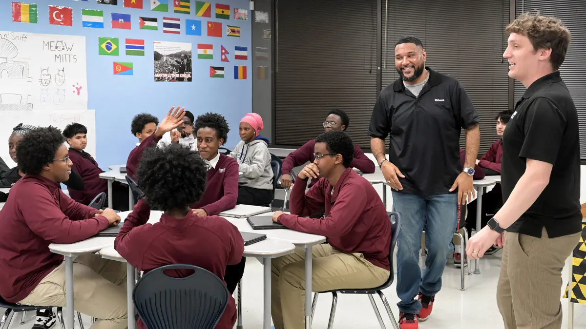 Two men with group of high school students in classroom.