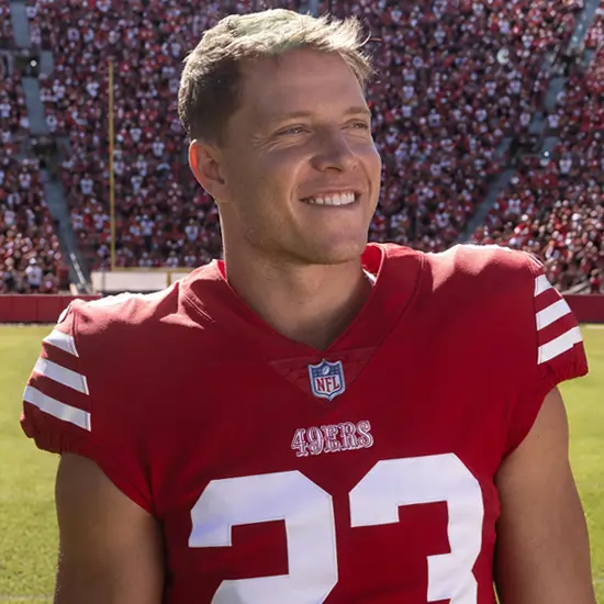 Christian McCaffrey on a football field, wearing a jersey and smiling