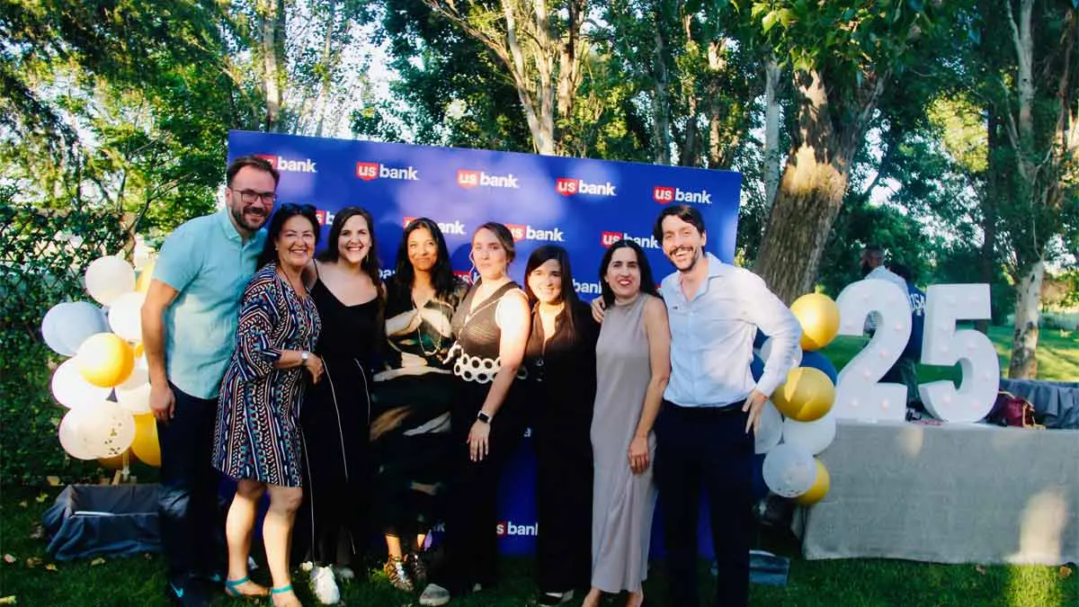 Photo of a group of about eight people gathered in front of a U.S. Bank sign and 25 