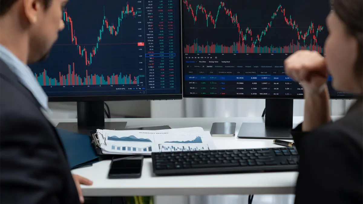 Photo of the backs of a man and woman looking at a multi screen financial display
