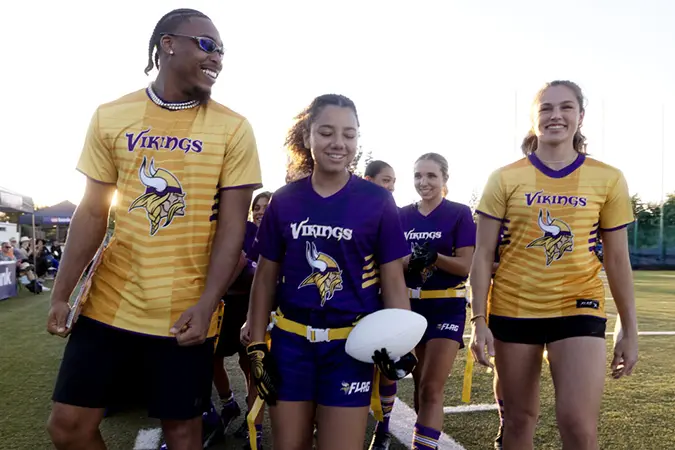 Flag football ambassadors Jusin Jefferson and Izzy Geraci walk down the football field with a team of kids.