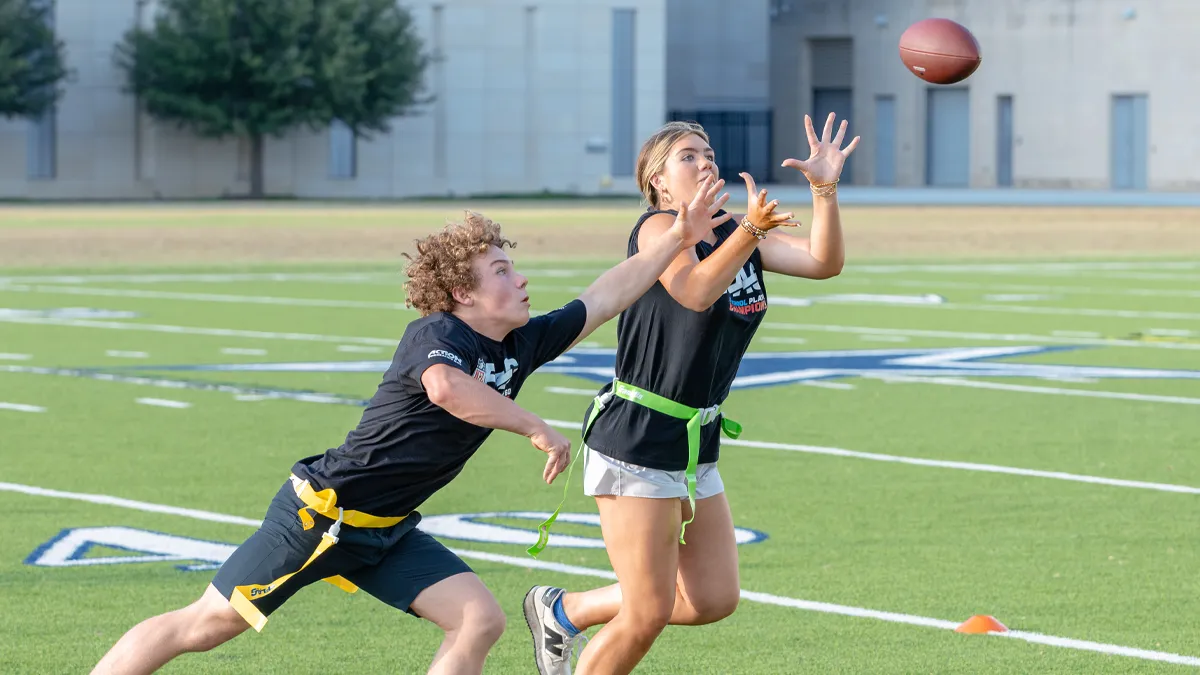 Two flag football players, a receiver and defender, trying to catch a ball that's in the air.