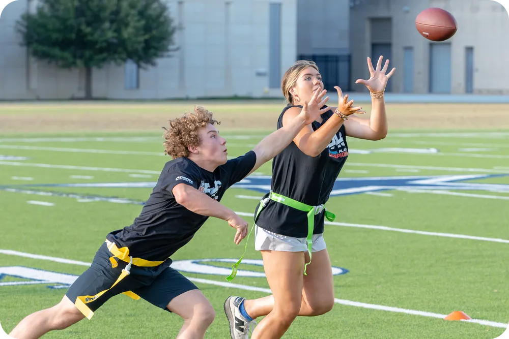 Two flag football players from opposing teams running to catch a ball in the air. 