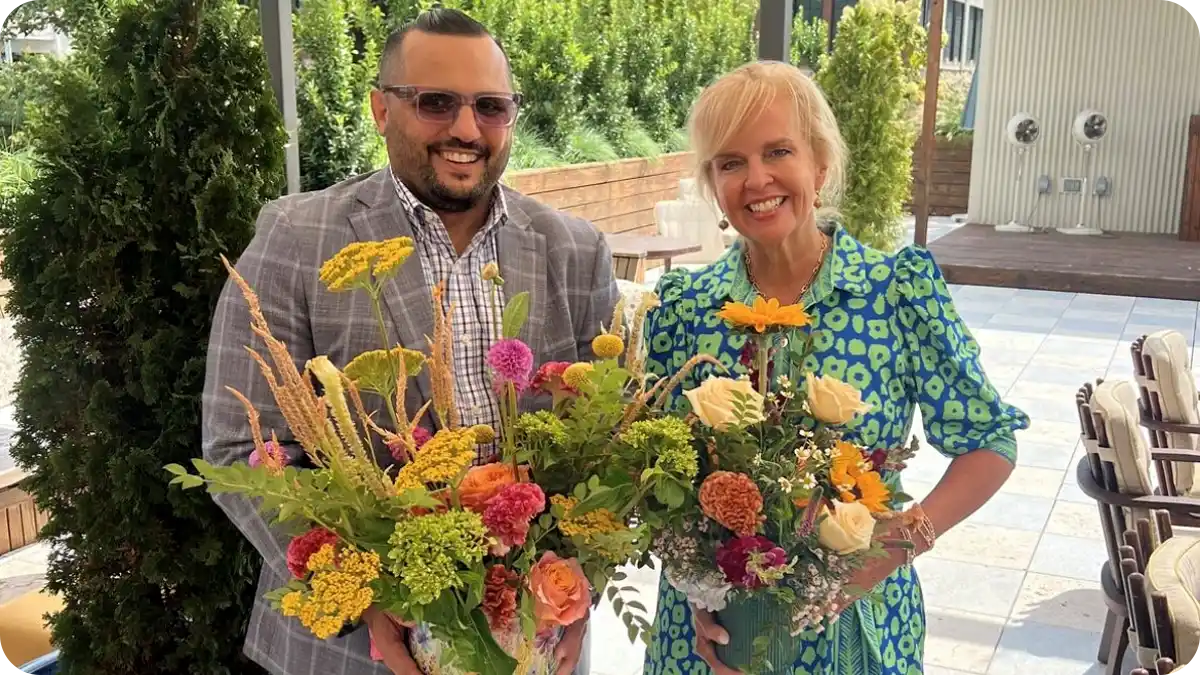 A man and woman standing together and each holding a floral arrangement.