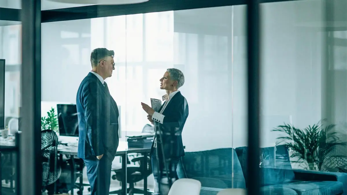 Photo of two a business man and woman standing and talking in a corporate conference room