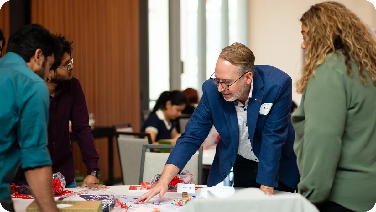Two people standing over a table with others seated.