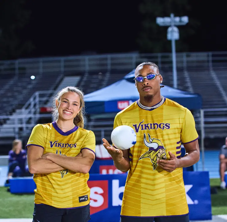 Justin Jefferson and Izzy Geraci in yellow shirts with purple accents. Izzy has her arms crossed, while Justin holds a white football.