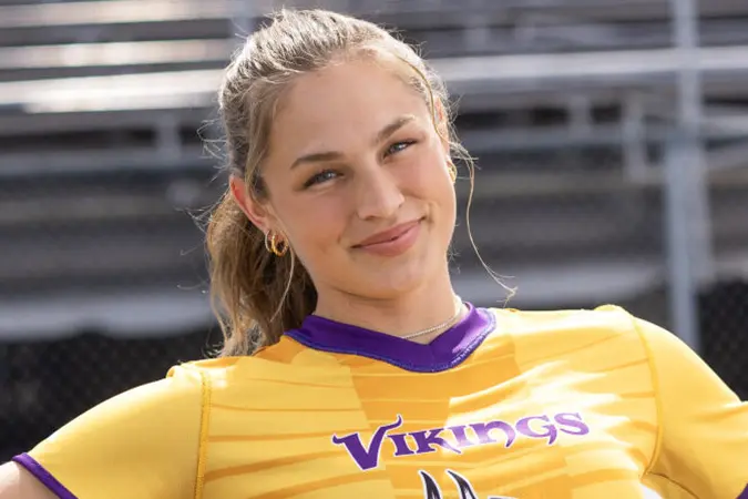 Izzy Geraci leans back on a bench on the sidelines and smiles.