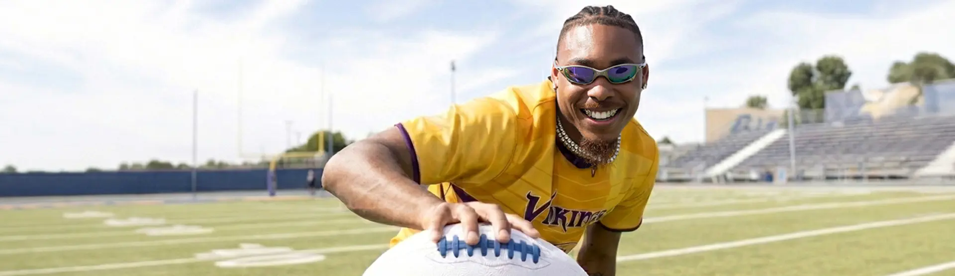 Minnesota Viking, Justin Jefferson smiles with an outstretched arm toward the camera holding a football.