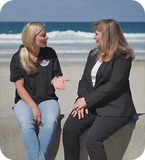 Two women sitting on a wall in front of the ocean.