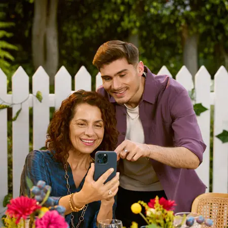 Un hijo le muestra algo a su mamá en su teléfono mientras están afuera en un jardín.