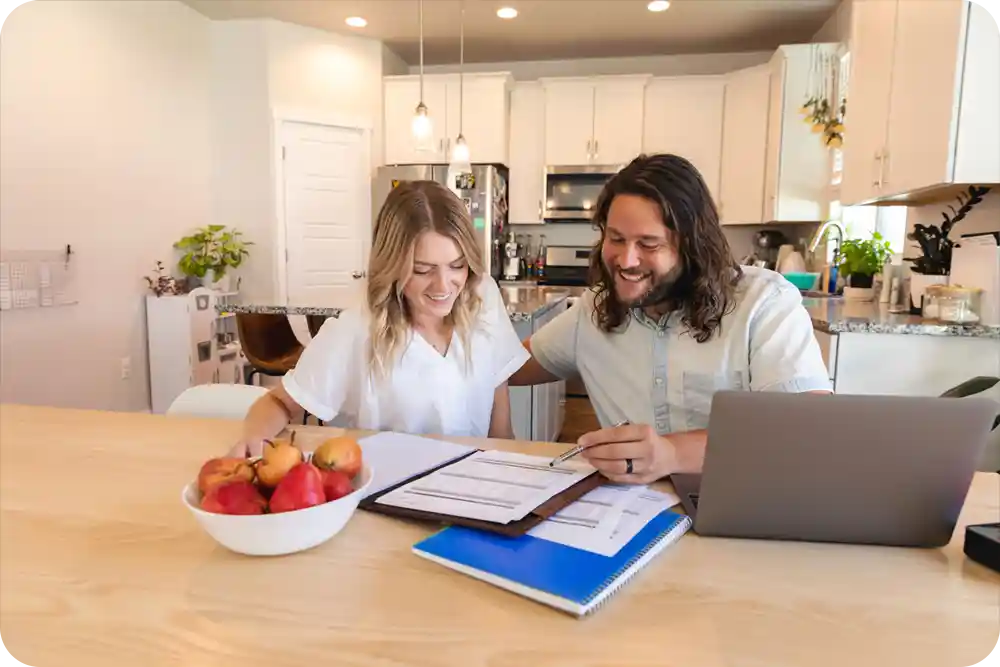 A man and woman sitting at a kitchen table in their house looking at paperwork