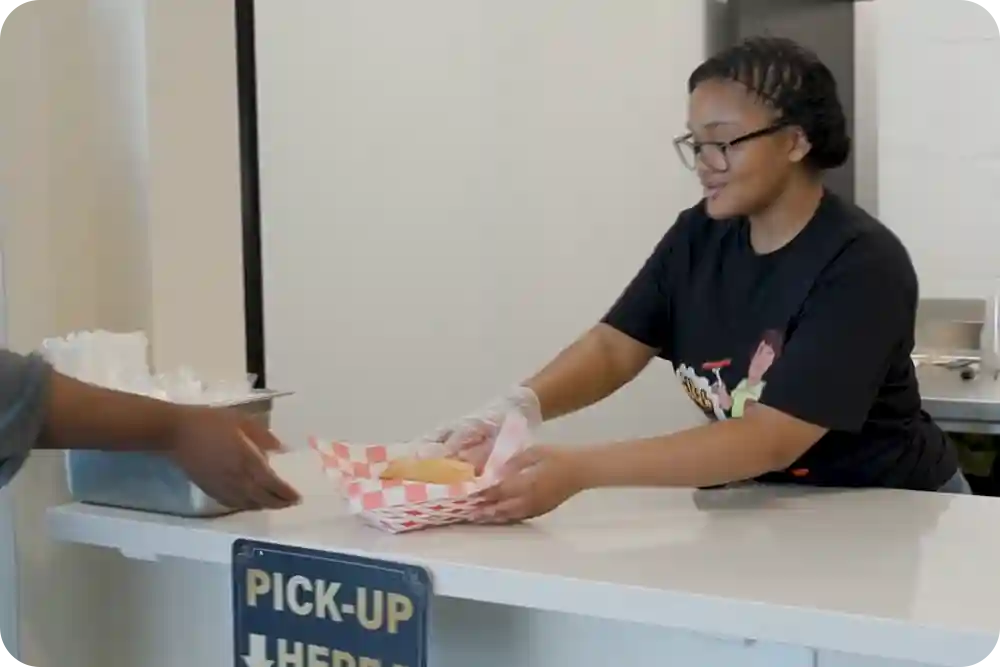 A woman behind a restaurant counter handing over a meal