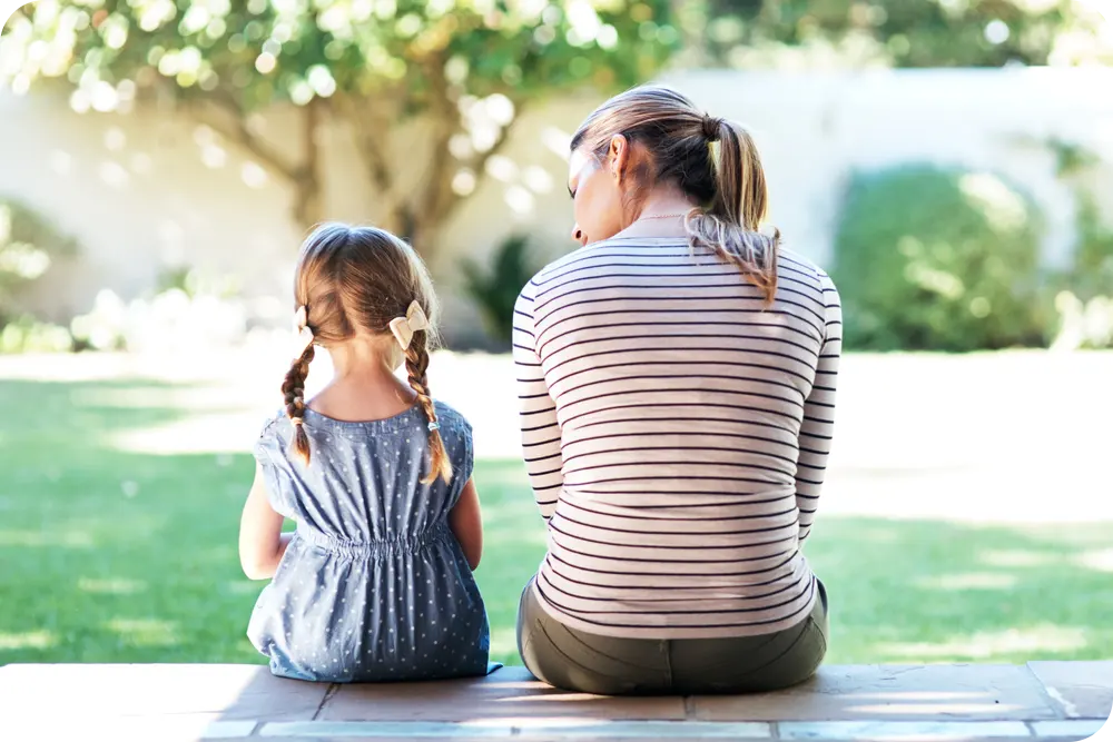 A woman and girl sitting on a porch with their backs to the camera.