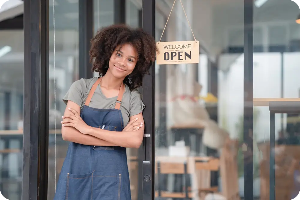 Woman standing front of a store with an "Open" sign in the window.