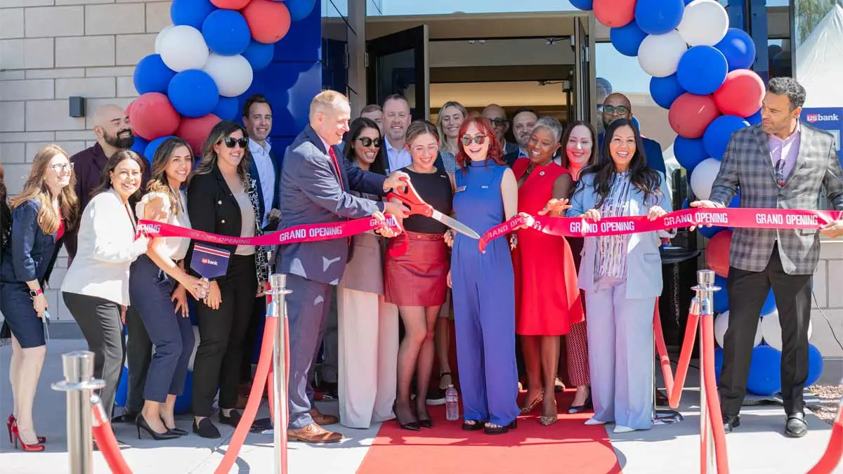 Group of people cutting a giant ribbon outside of a bank branch.