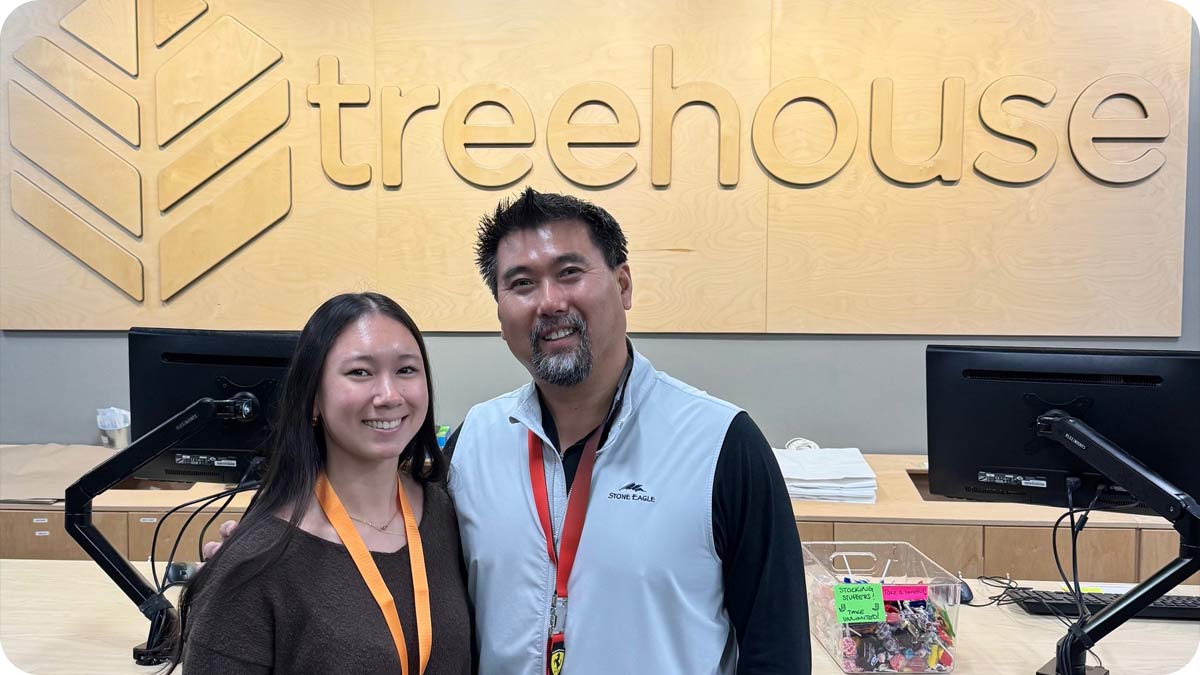 Photo of father and daughter smiling at the camera in front of a sign that says Treehouse.