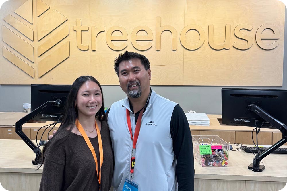 A man and his daughter smiling at camera in front of sign that says Treehouse