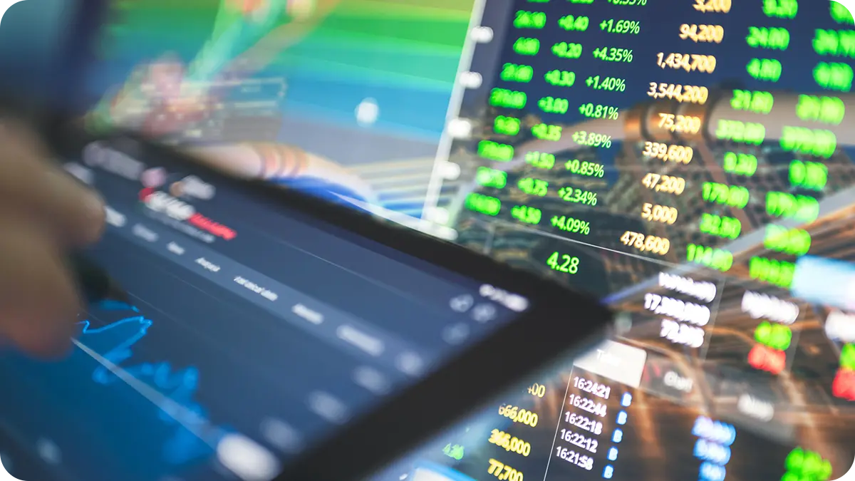 Someone using a tablet in front of a monitor with a lot of data on both.