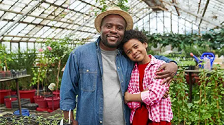 Hombre en un invernadero abrazando por la espalda a un niño.