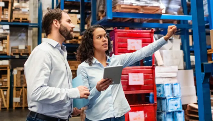Hombre y mujer en una bodega de inventario. Mujer sosteniendo una tableta.