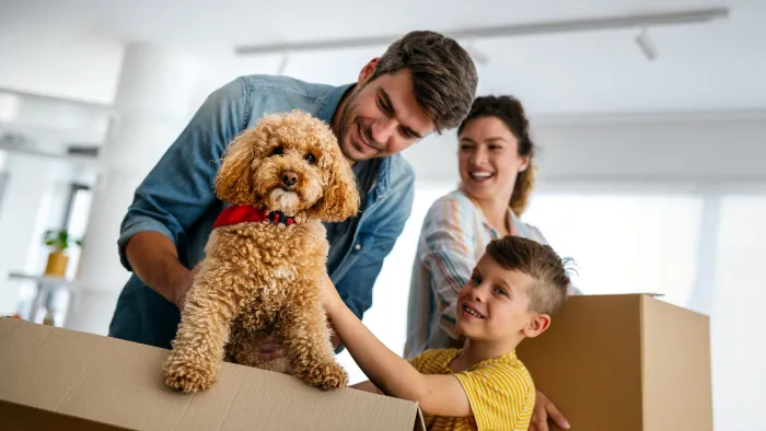 Family of three smiling with dog and moving boxes.