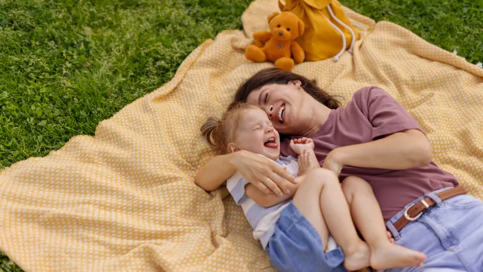 Photo of a mother and daughter giggling on a blanket