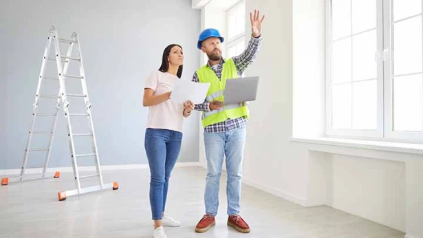 Two people working together, reviewing construction plans and documents on a laptop.