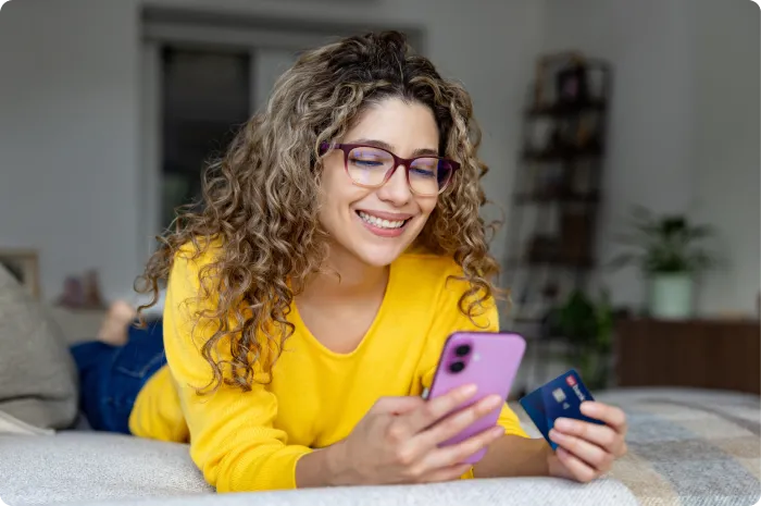 Person reclining on bed using phone while holding card