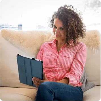 Woman in pink striped shirt sitting on couch viewing tablet