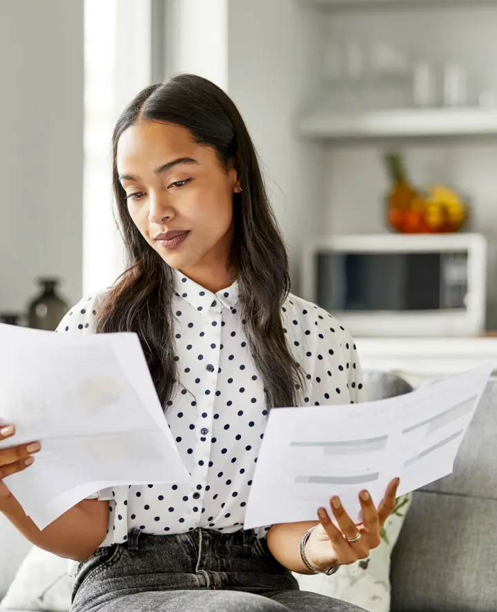 Woman sitting at home looking at paperwork in both hands