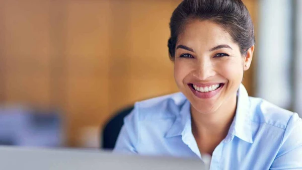 Smiling individual in a light blue collared shirt, set against a blurred indoor background.