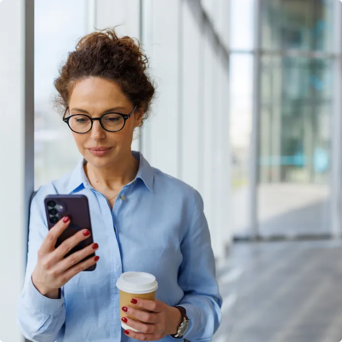 Digital consumer paused in an office walkway with coffee using a smartphone