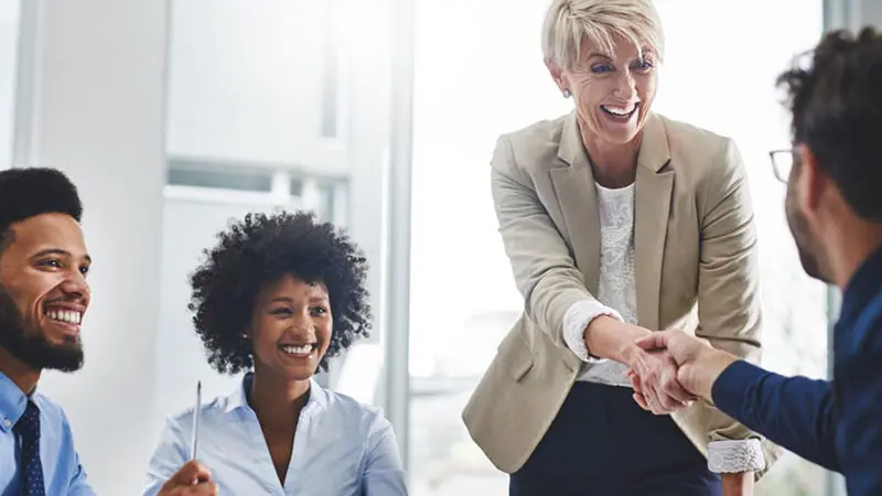 A woman in a suit shakes hands with a man at a business meeting, after discussing questions choosing a financial custodian institution.