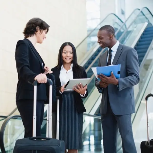 Three people looking at a tablet next to an escalator assessing corporate travel management.