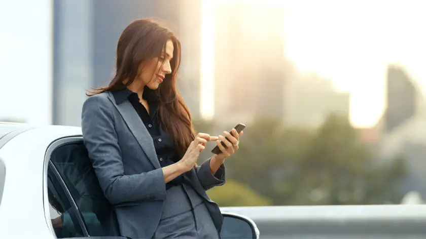 Woman in suit leaning against car looking at phone for ETF services