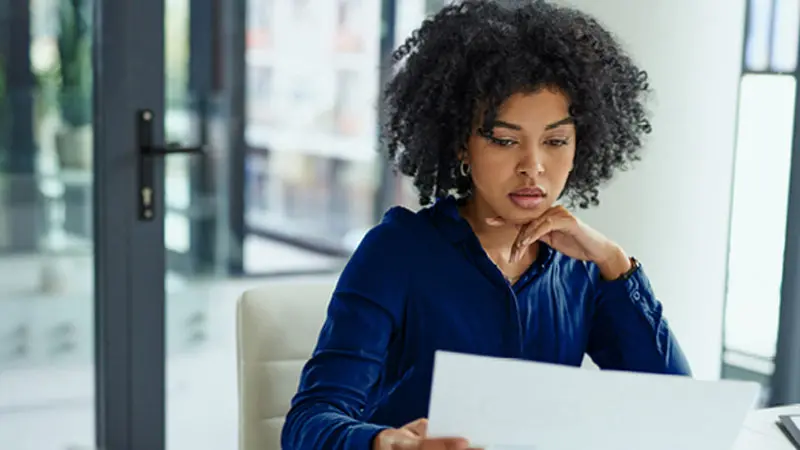 Woman reviewing two manual expense reports – a travel expense report and a corporate expense report.