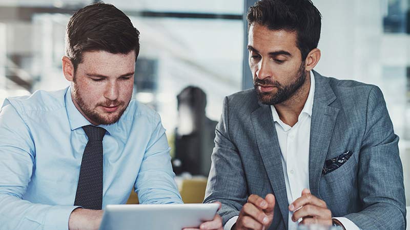 Two corporate colleagues looking at fraud prevention tips on a tablet device