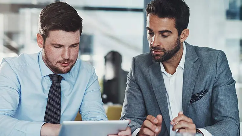 Two corporate colleagues looking at fraud prevention tips on a tablet device
